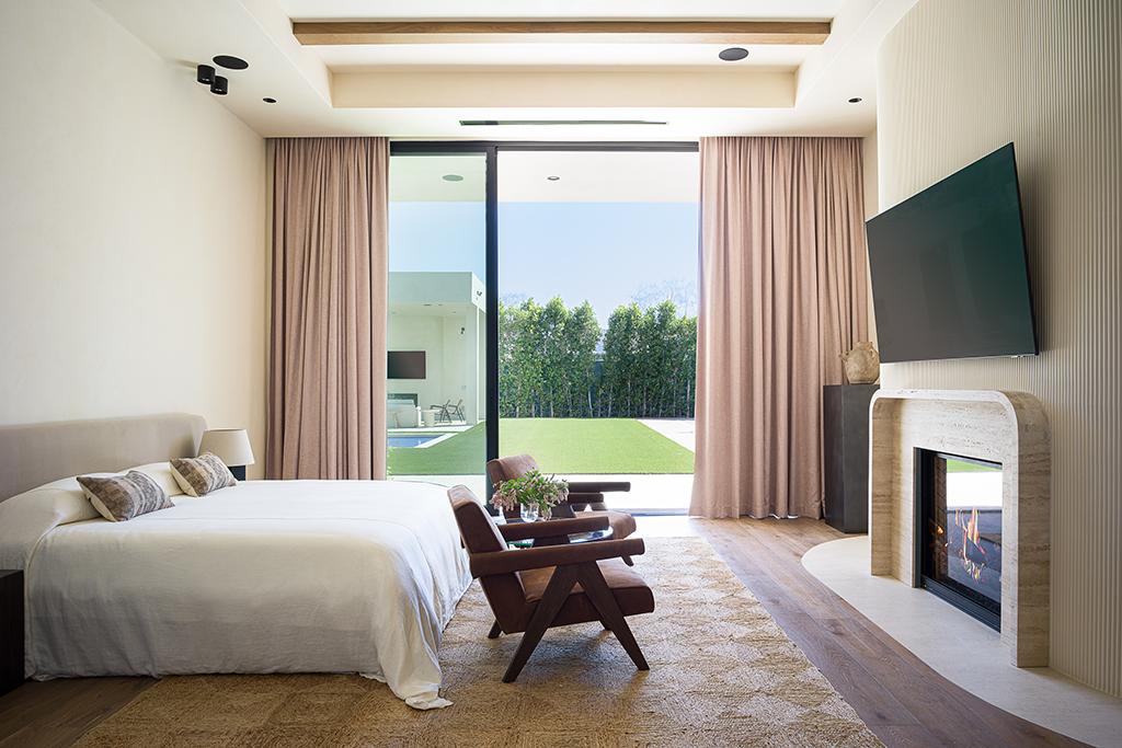 Primary bedroom with travertine fireplace and slide doors leading to the lawn and backyard