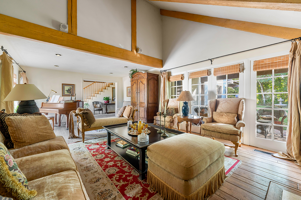 Living Room of Main Home | The Agency Journal Cozy sitting room with view out French doors to the patio and lawn with a piano at the far end