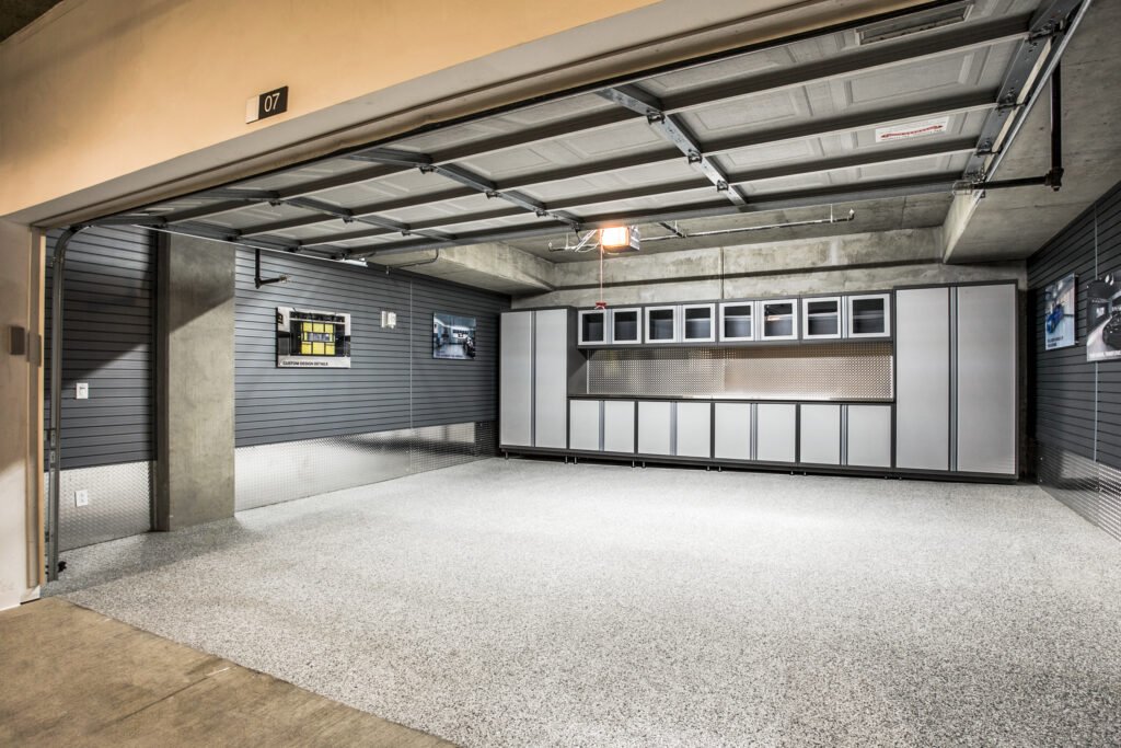 Modern, well-organized garage with grey epoxy speckled floor, sleek storage cabinets, slatted walls, and bright lighting—clean, functional, and high-end.