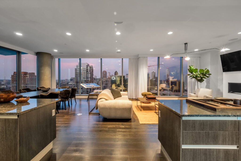 Spacious modern penthouse living room with hardwood floors, shuffleboard table, “LOVE” sculpture, and skyline views through floor-to-ceiling windows in Dallas.
