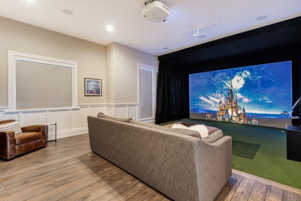 Modern living room with high ceilings, large windows overlooking a lake, a dark leather sectional, wooden beams, and a mix of rustic and contemporary decor.