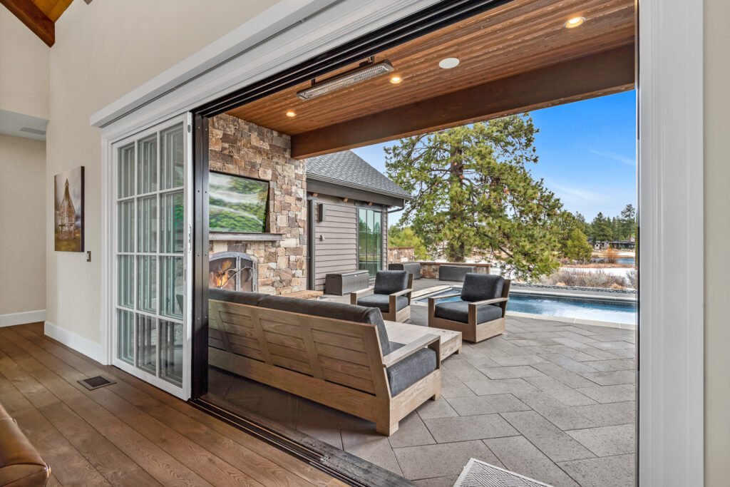 Modern kitchen and dining area with dark wood table, wine storage, wood-beam ceiling, and natural light from large windows.