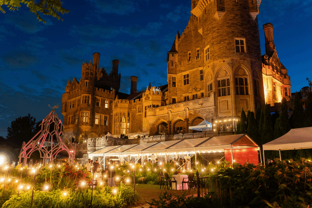 Nighttime outdoor event in the gardens of a grand illuminated Gothic-style castle.