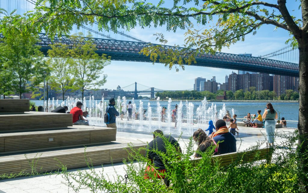 Brooklyn, NY / USA - 8/20/20: Landscape view of Domino Park's fountain and seating steps. The East River and Williamsburg Bridge in the distance.