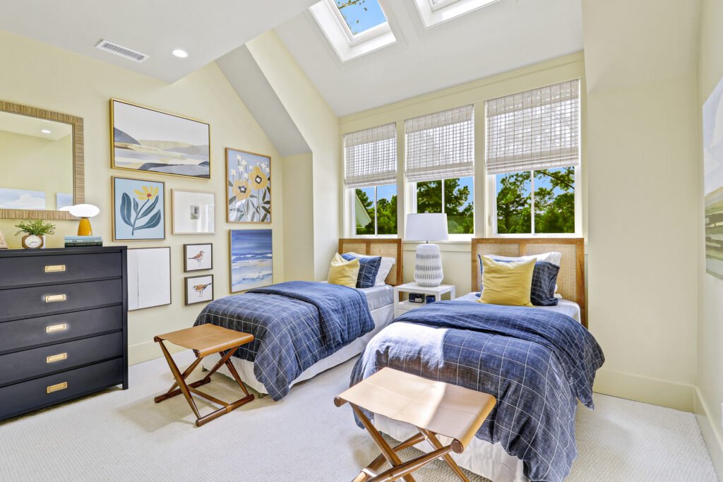 Twin guest bedroom from HGTV Dream Home 2025 with light yellow walls, blue accents, and two neatly made twin beds. Features include a whimsical gallery wall, smart storage solutions, and an attached modern bathroom, creating a warm and inviting retreat.