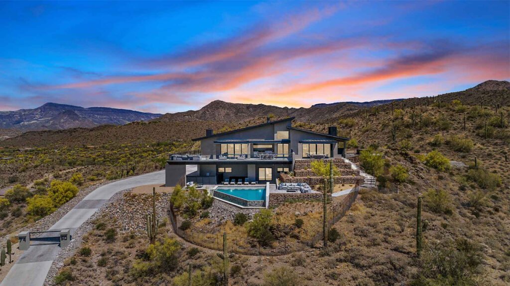 Modern house with a swimming pool on a desert mountainside at sunset.