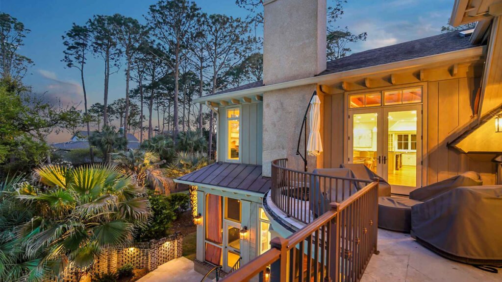 Hilton Head Island house at dusk with a large balcony and lush tropical landscaping.