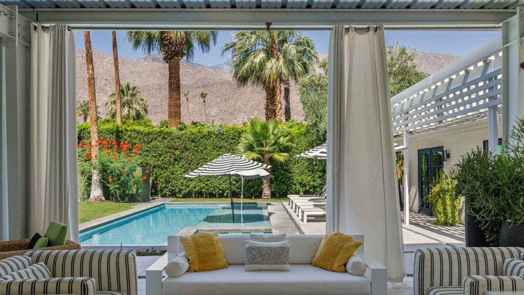 A scenic view of a resort-style backyard with a pool, palm trees, and mountains in the background.