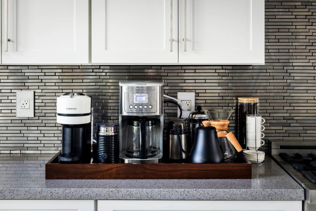 A modern, well-organized coffee station featuring a variety of coffee makers and accessories on a kitchen counter with a tiled backsplash.