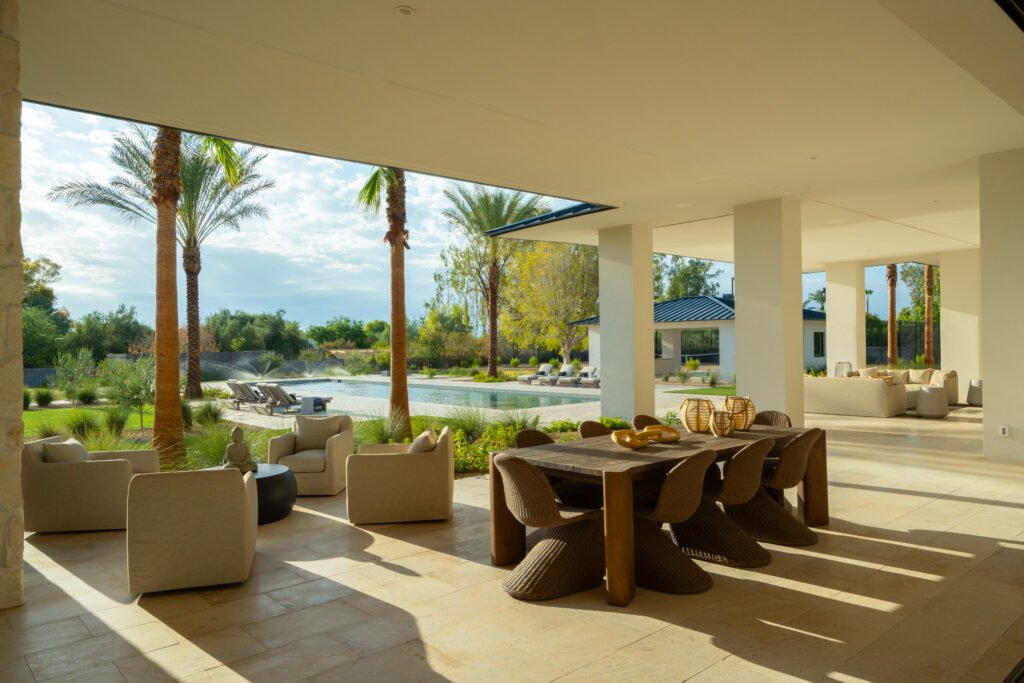 Expansive covered patio with outdoor dining, lounge area, overlooking pool, palm trees, and desert landscape.