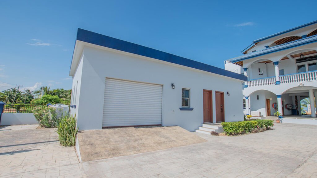 The exterior of a luxury Belize beach house featuring a garage, two brown wood doors, and tropical landscaping.