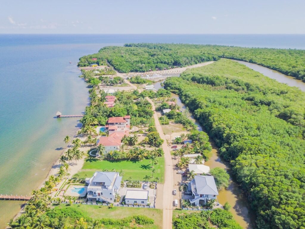  An aerial view of a luxury Belize beachfront property featuring two large houses, a pool, and lush tropical landscaping between the Caribbean Sea and a river.