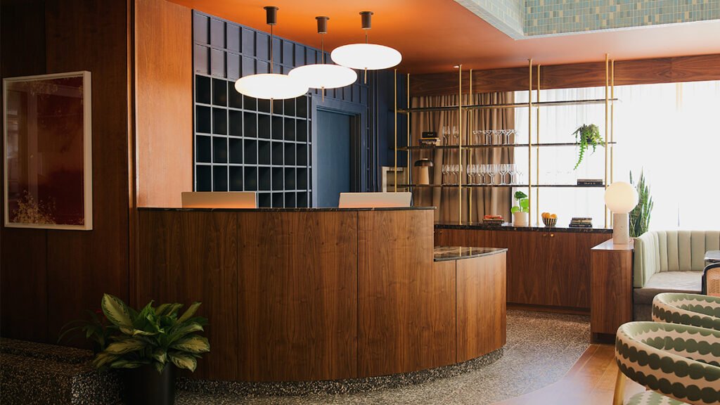 Mid-century modern hotel lobby with a curved wooden reception desk, and designer pendant lights.