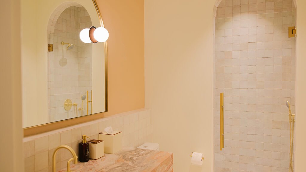 Modern hotel bathroom at the Municipal Grand Hotel in Savannah with a pink marble vanity, arched mirror, and gold fixtures.