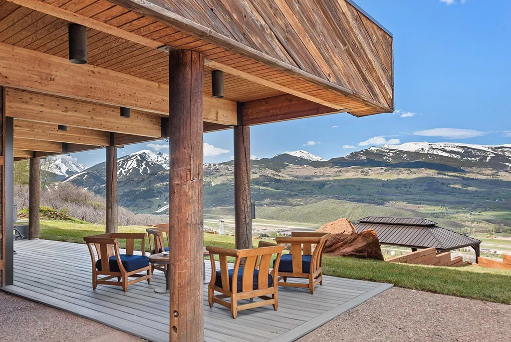 Rustic-contemporary covered deck with outdoor seating, views of an airfield and distant mountains.