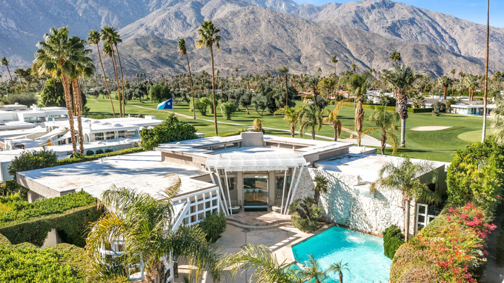 A stunning mid-century modern luxury home in Palm Springs, California, featuring an integrated courtyard pool and expansive views of a lush green golf course and rugged mountains.