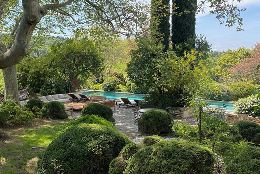 Luxury Provencal garden with a swimming pool, sun loungers, boxwood topiary, and tall Italian cypress trees.