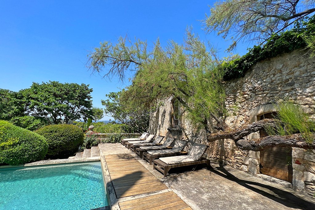 Luxury stone villa in Provence, France, featuring a poolside terrace with lounge chairs and manicured gardens.