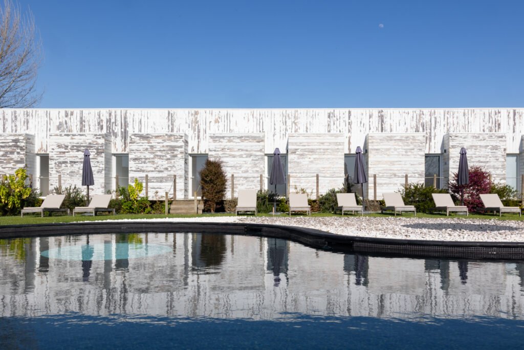 Modern eco-resort in Portugal featuring white weathered wood villas, sun loungers, and a large outdoor pool.