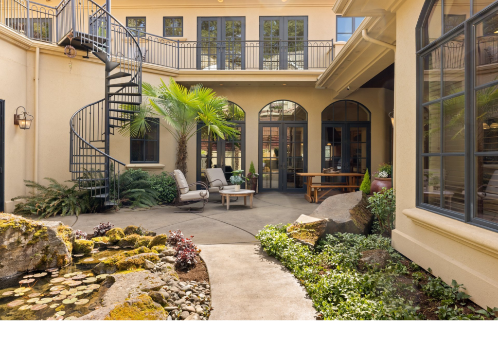 Mediterranean-style courtyard with a black iron spiral staircase, stone-rimmed koi pond, and palm tree.