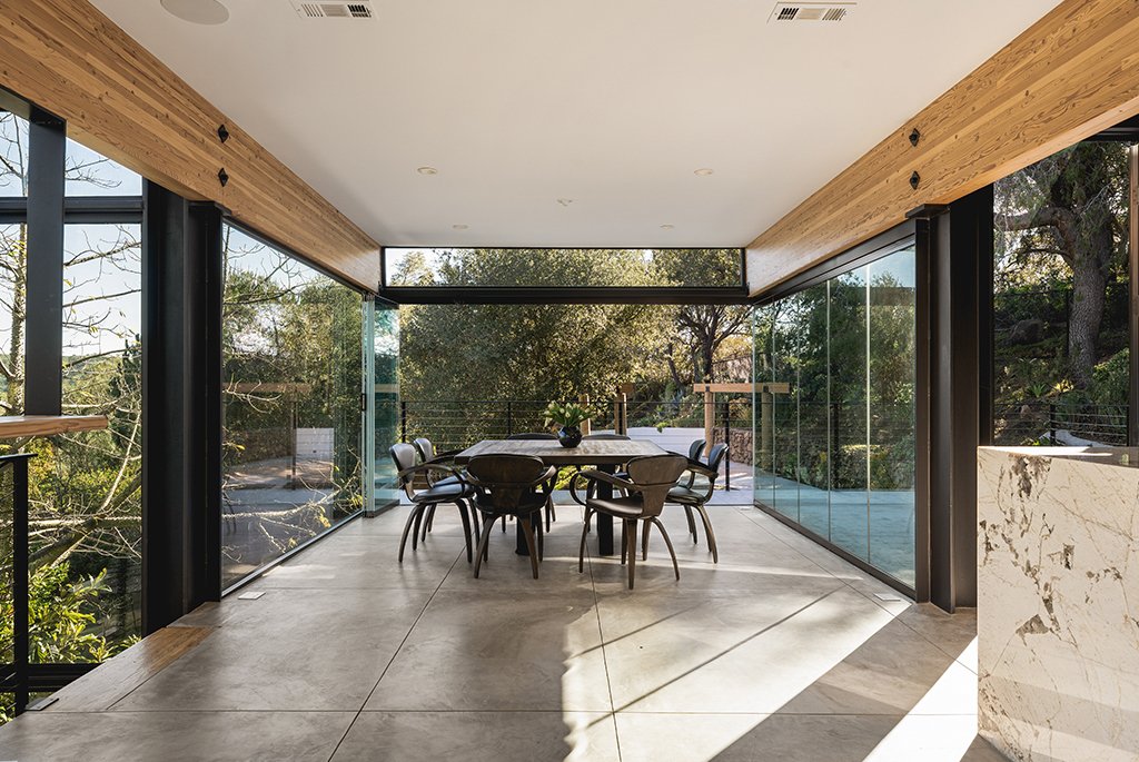Modern dining room by Finn Kappe in Malibu, featuring retractable floor-to-ceiling glass walls, a minimalist table set, and a seamless flow to an outdoor terrace with canyon views.