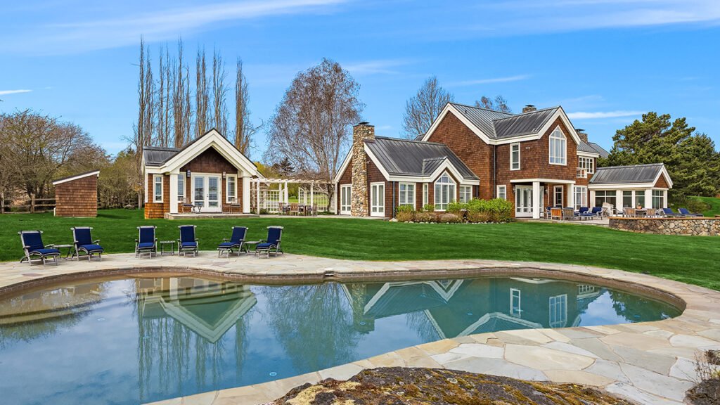 Luxury country estate backyard showing a swimming pool, lakeside lounge chairs, and an expansive lawn.