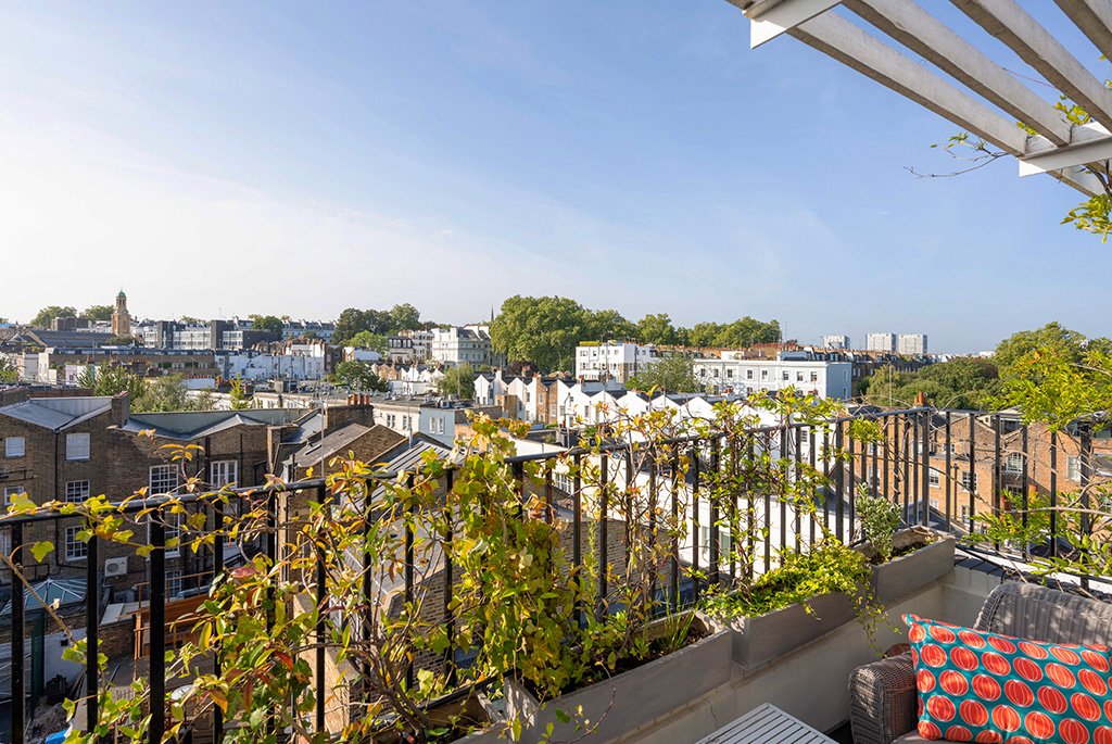 Rooftop terrace with a metal railing, green planters, and panoramic views of the city skyline.