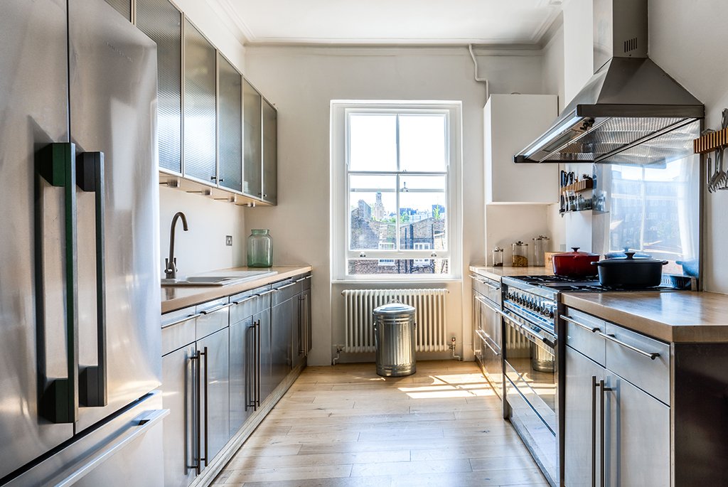 Modern galley kitchen with stainless steel cabinets, wood countertops, and a professional gas range.