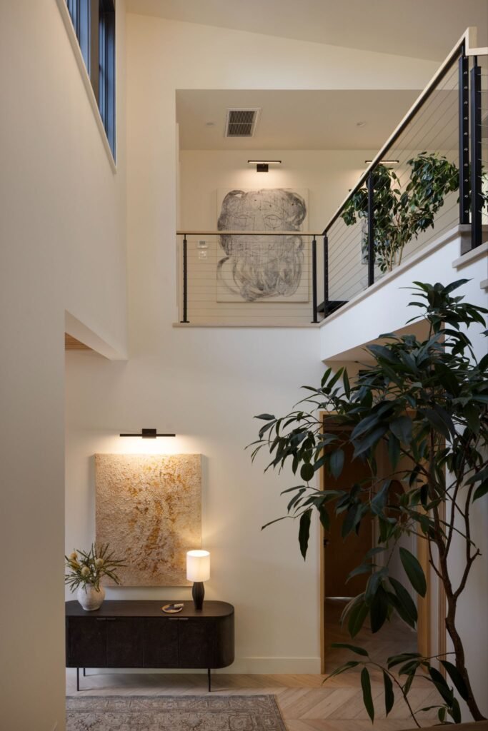 Double-height entryway foyer with a mezzanine overlook, cable railings, and light herringbone wood floors.