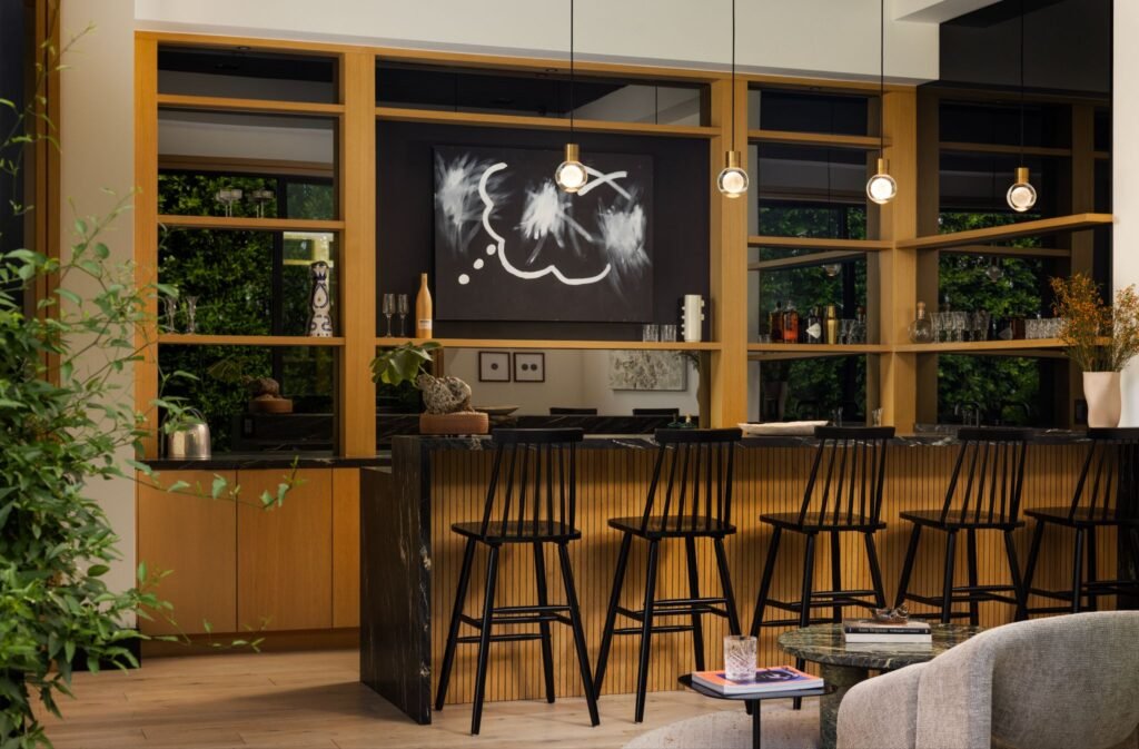 High-end home bar featuring a black marble island with gold veins, custom oak shelving, and modern pendant lights