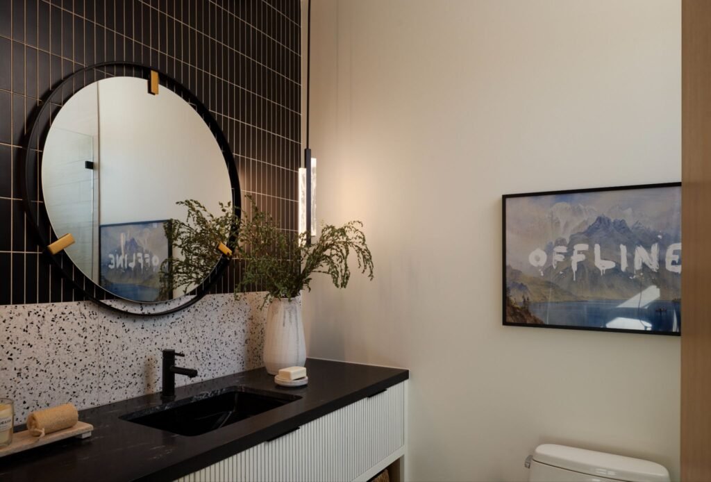 Modern powder room featuring a terrazzo backsplash, black vertical stacked tiles, and a large round mirror.