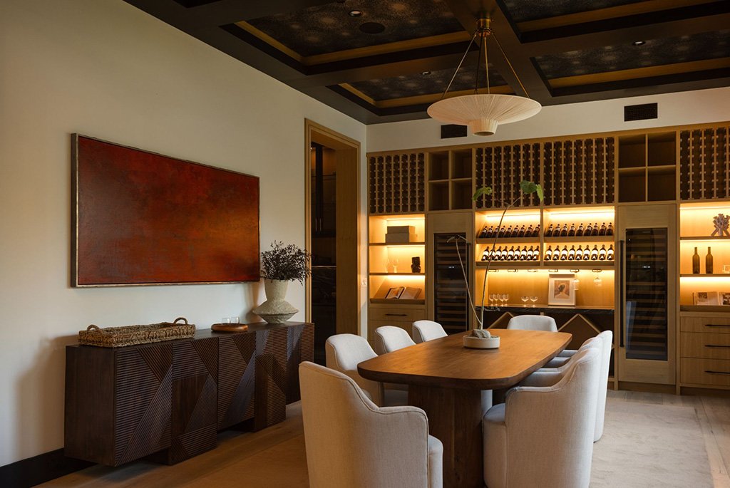 Luxury dining room featuring a large wood table, custom oak wine wall with integrated lighting, and a coffered ceiling.