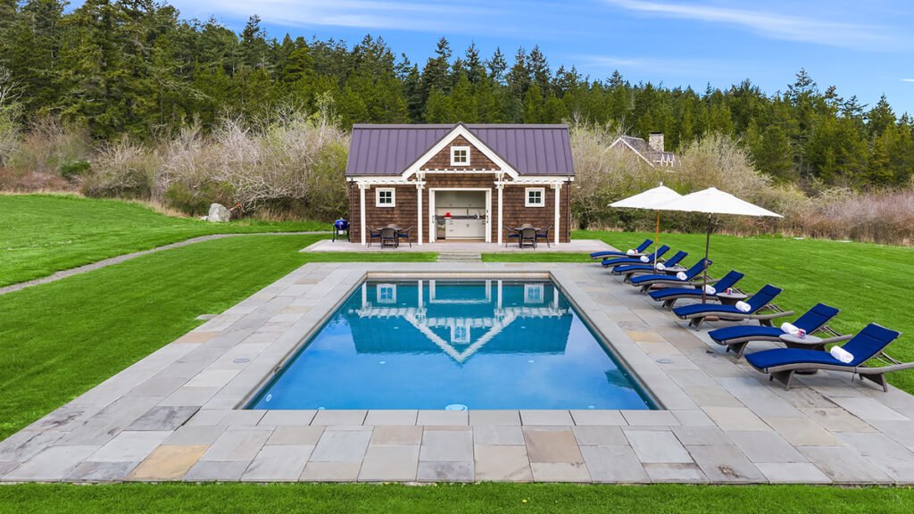 Luxury estate backyard pool area with a perfectly mirrored water reflection and manicured green lawns.