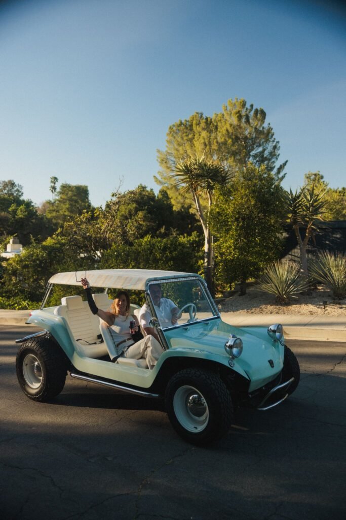 Vintage Meyers Manx dune buggy driven by a couple in a suburban neighborhood.