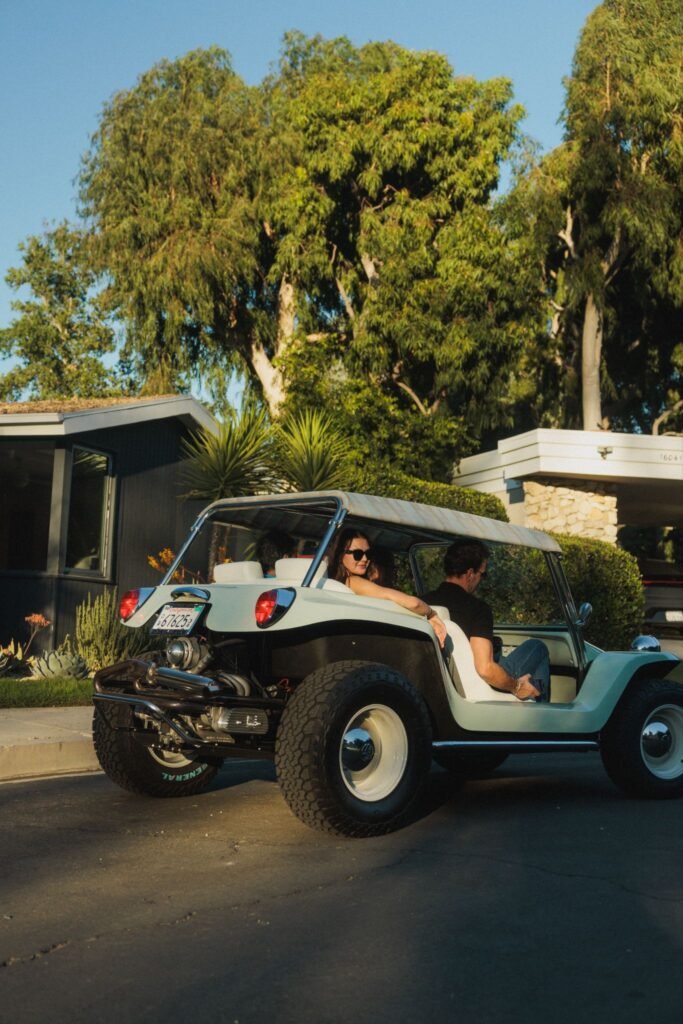 Vintage Meyers Manx dune buggy driving past a mid-century ranch house