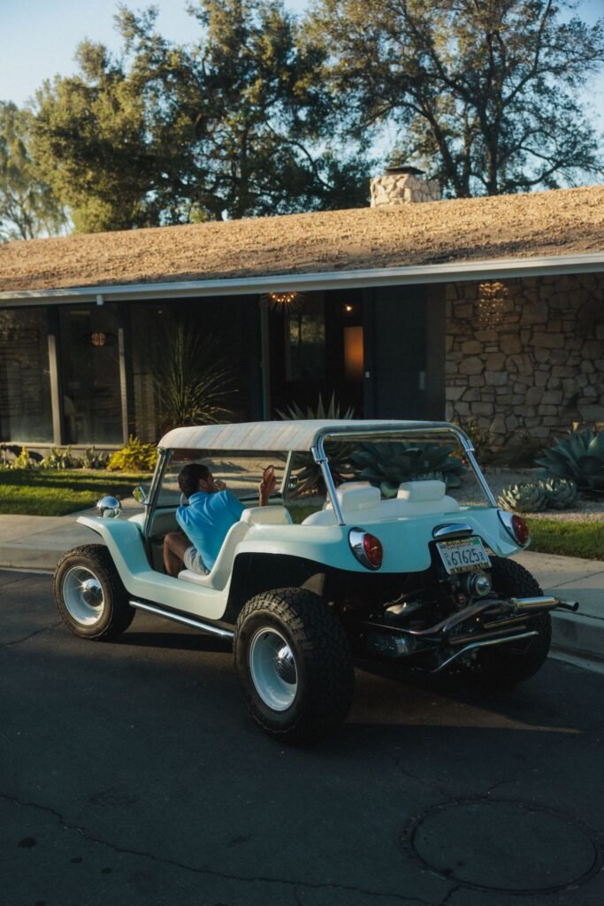 Retro light blue dune buggy outside a mid-century modern stone home.