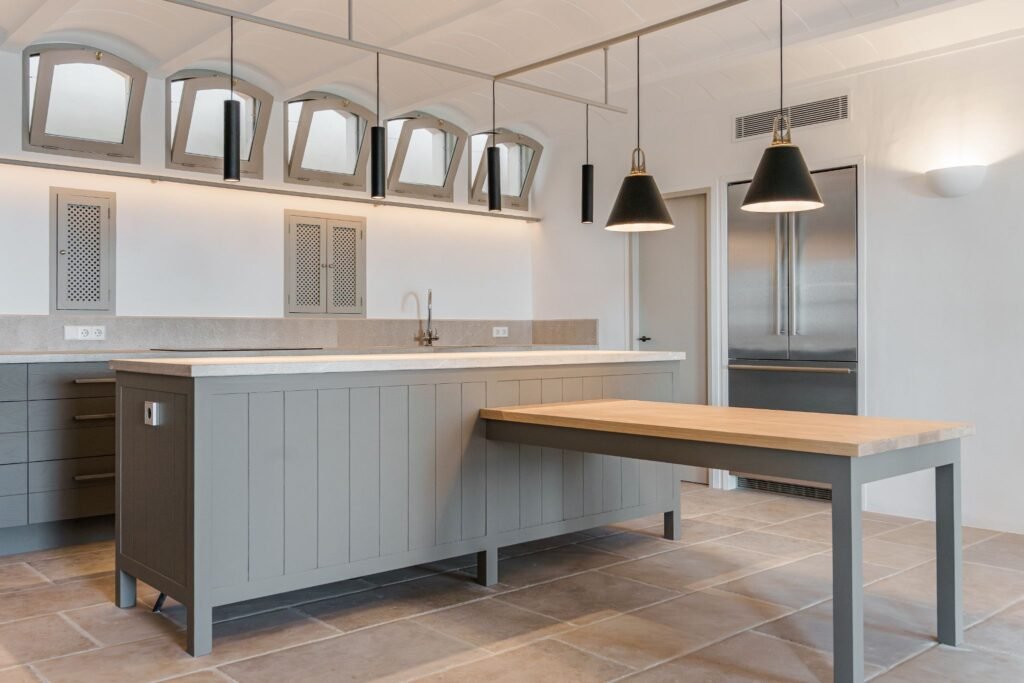 Modern luxury kitchen featuring a gray island with an integrated wood dining table extension and black pendant lighting.
