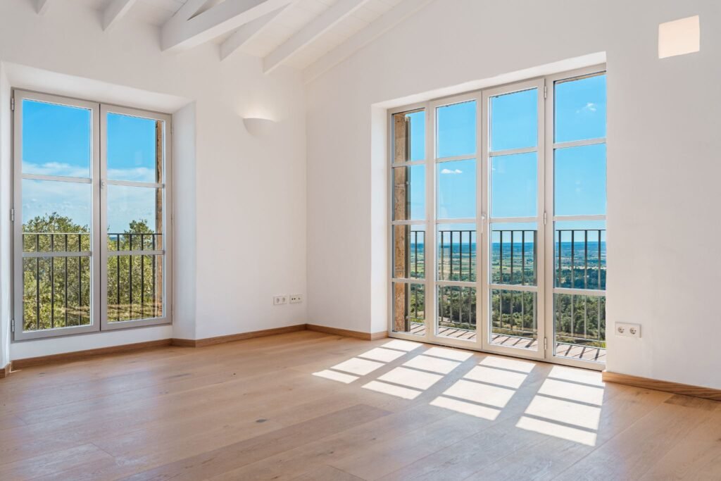 Bright luxury bedroom interior with light oak hardwood floors and large French doors opening to panoramic countryside views.