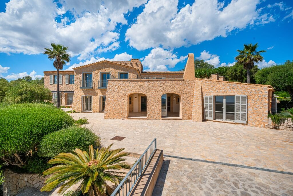 Luxury Mediterranean stone villa facade with arched entryways, private balconies, and a paved courtyard.