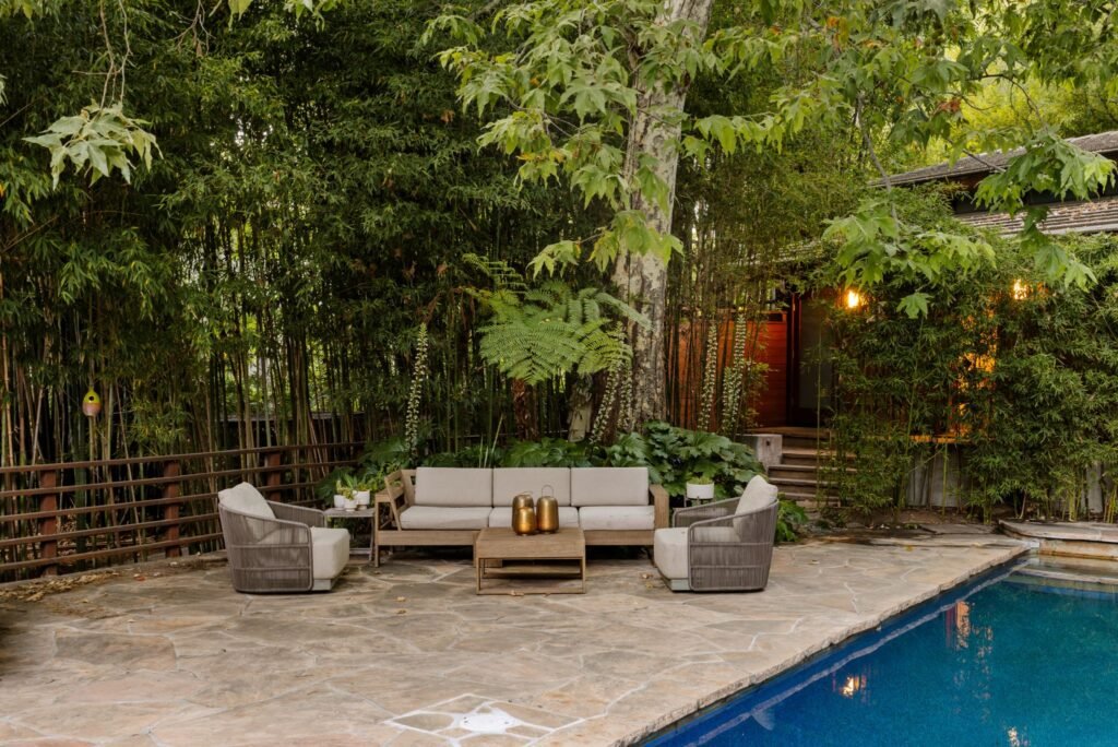 Luxury backyard oasis featuring a flagstone patio pool deck with upscale outdoor lounge seating, a sparkling swimming pool, and a private bamboo forest backdrop.