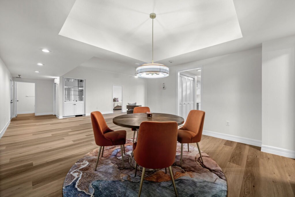 Spacious open-concept basement or bonus room with a recessed tray ceiling, modern drum chandelier, a round wooden dining table, and light hardwood floors.