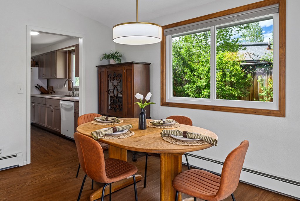 Bright dining room with an oval wooden table, cognac leather chairs, a modern drum pendant light, and a large window looking out to a green backyard.