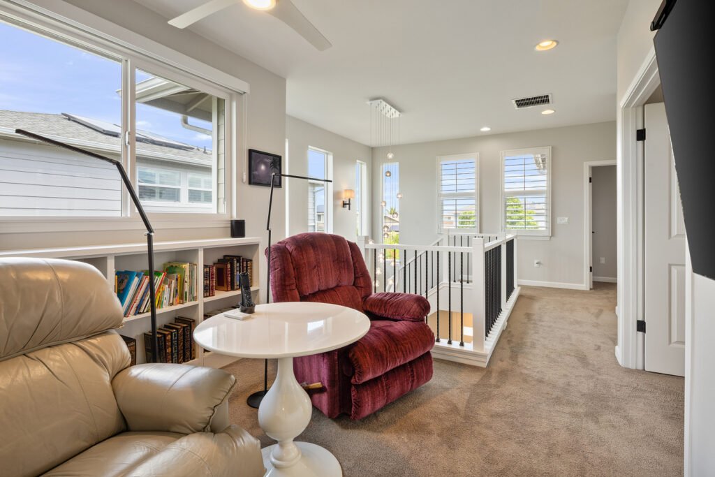 Second-floor loft and landing area with carpeted floors, built-in bookshelves, an open staircase railing, and bright windows with plantation shutters.
