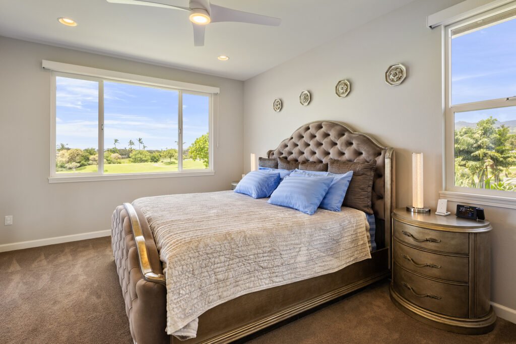 Primary bedroom suite with a tufted headboard, carpeted floors, modern ceiling fan, and large windows overlooking a golf course.