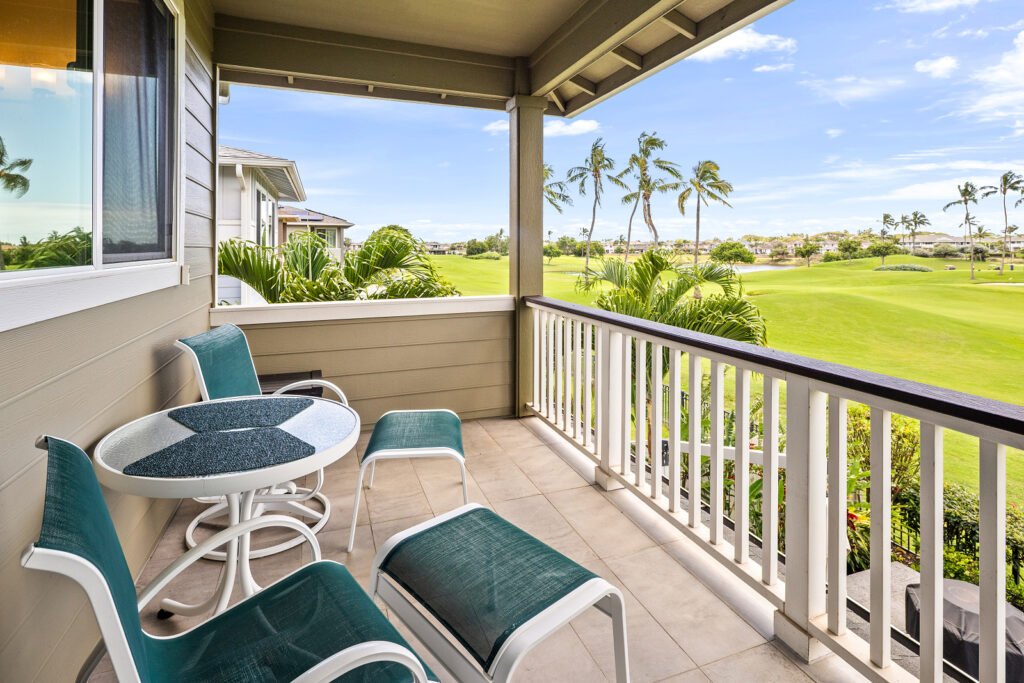 Covered second-floor balcony with outdoor seating, a small dining table, and panoramic views of a lush golf course and palm trees.