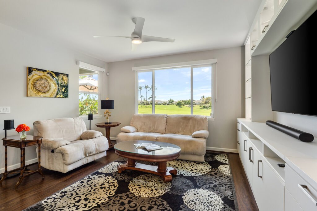 Bright living room with dark wood floors, large custom media built-in console, and windows overlooking a golf course.