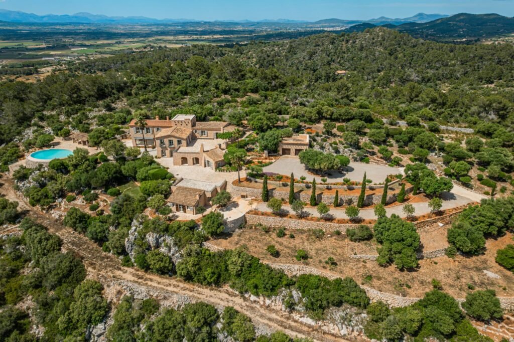 Aerial drone view of a luxury Mediterranean hilltop estate with stone villas, a round swimming pool, and panoramic mountain view