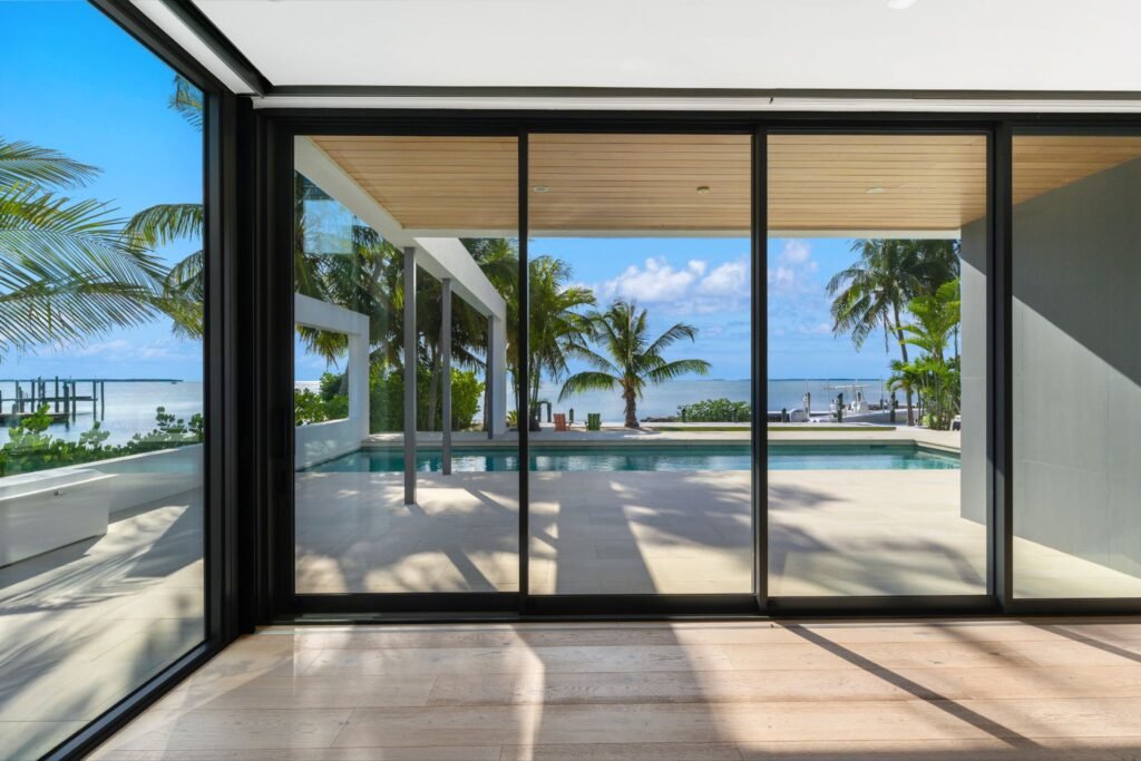 Floor-to-ceiling continuous glass windows at 19 Avacado Street in Islamorada, framing panoramic views of the 50-foot saltwater lap pool and the sunset-facing bay.