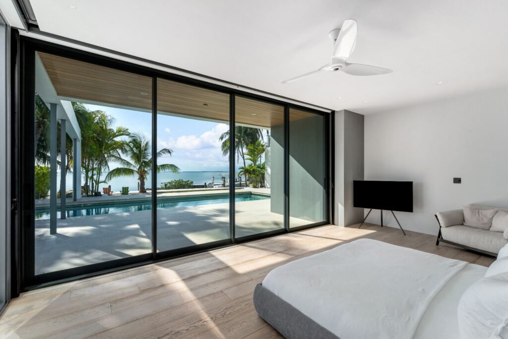 First floor primary suite at 19 Avacado Street in Islamorada, featuring floor-to-ceiling glass windows with direct views of the 50-foot saltwater lap pool and bay.