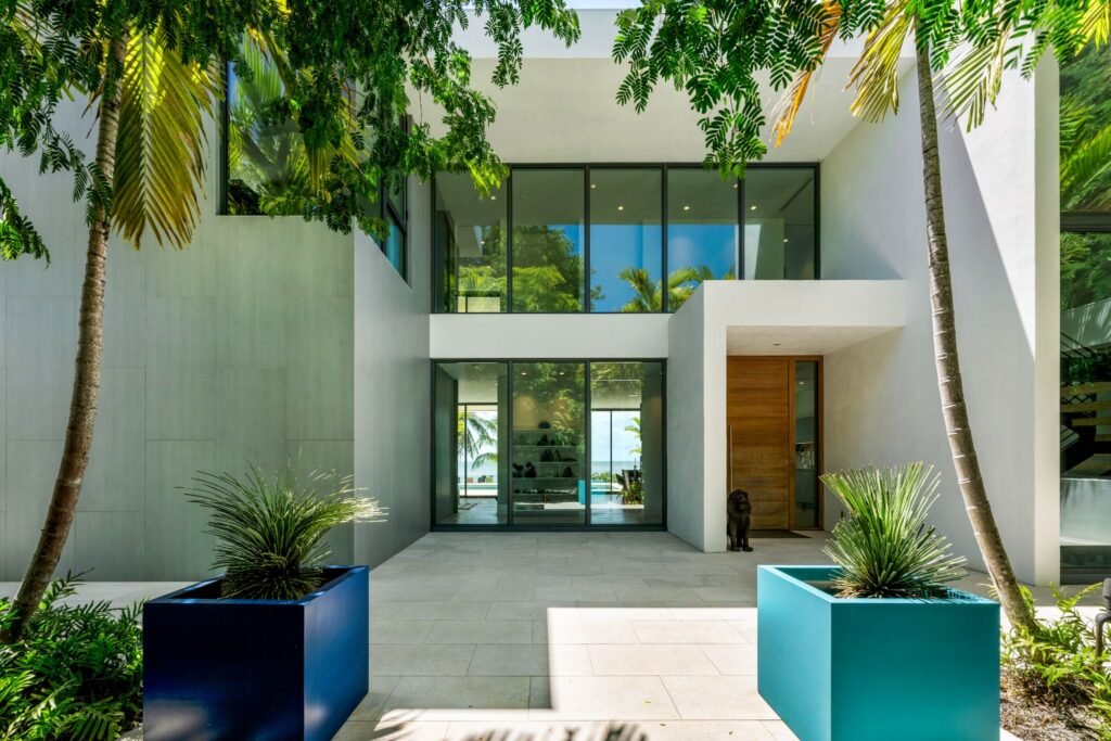 Modern entry foyer and 12-foot wooden door at 19 Avacado Street in Islamorada, showing the coastal modernism architecture with floor-to-ceiling windows and tropical palm framing.
